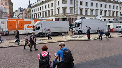 Ansicht des Landtagsgebäudes. Das Gebäude wird fast gänzlich von Ü-Wagen diverser Sendanstalten verdeckt. Im Vordergrund sitz ein Paar auf Stufen und isst ein Eis.