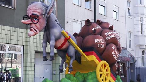 Ein Karnevalswagen beim Rosenmontagszug in Düsseldorf zeigt als Pappmascheefigur CDU-Chef Merz als Esel. Er zieht einen Karren mit Säcken, unter anderem zum Schuldenpaket.