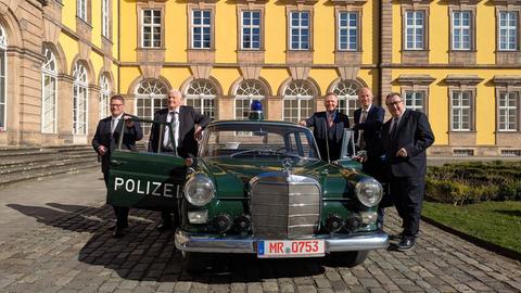 Fünf Männer in Anzügen an einem Polizei-Oldtimer 