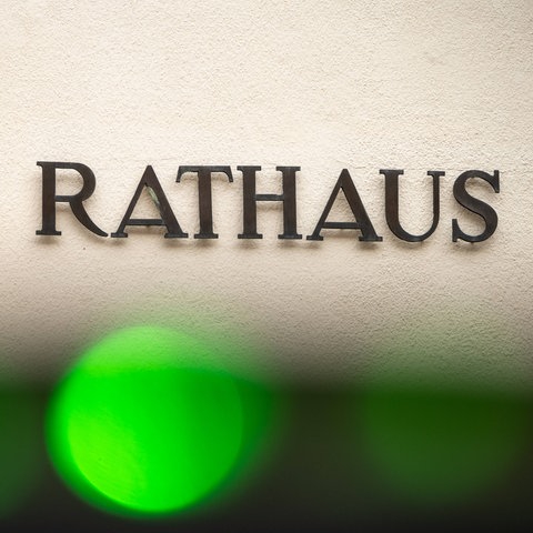 Foto: Das Wort "Rathaus" - einzelne Metallbuchstaben - an einer Hauswand. Am seitlichen Rand ist etwas Sandstein zu sehen. Am vorderen Rand ein grüner Lichtfleck, vermutlich von der Kamera.