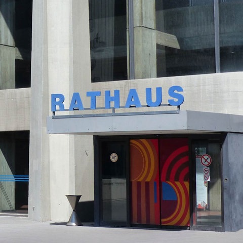 Zeitgenössisches Gebäude aus Beton mit farbigen Flächen. Über der Eingangstür steht groß "Rathaus". 