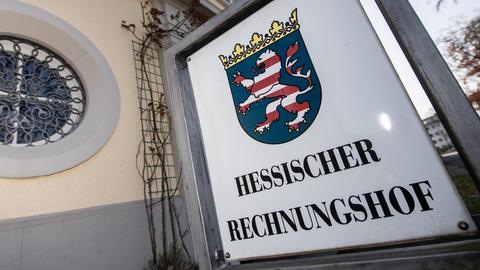 Schild mit der Aufschrift "Hessischer Rechnungshof", darüber ein Hessenwappen, vor einem Gebäude.