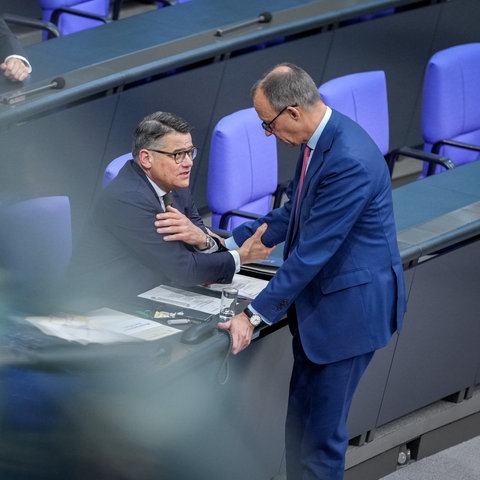 Boris Rhein und Friedrich Merz reden in einem ziemlich leeren Bundestag miteinander. Rhein sitzt, Merz steht.