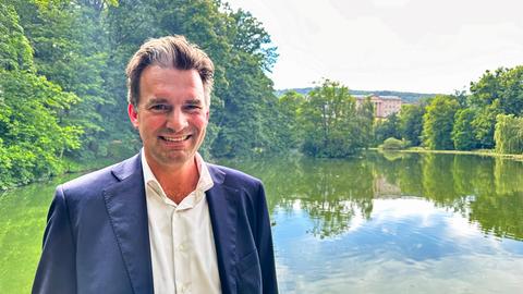 Schoeller steht vor dem Lac und lächelt, im Hintergrund das Schloss Wilhelmshöhe