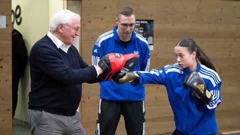 Bundespräsident Frank-Walter Steinmeier (l) schützt sich beim Boxtraining mit speziellen roten «Handpratzen», ein Mädchen boxt rein