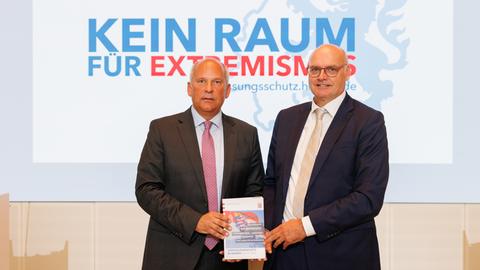 Roman Poseck und Bernd Neumann präsentieren den Verfassungsschutzbericht, beide stehen vor dem Schriftzug "Kein Raum für Extremismus"