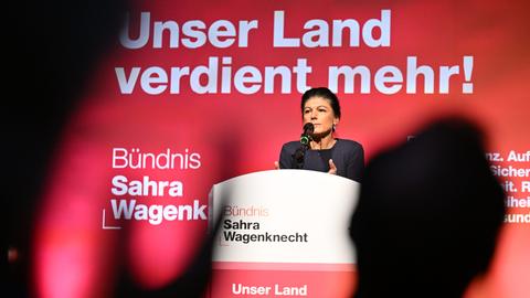 Sahra Wagenknecht steht auf einer Bühne und hält eine Rede, im Vordergrund sind Silhouetten von Zuhörern zu erkennen