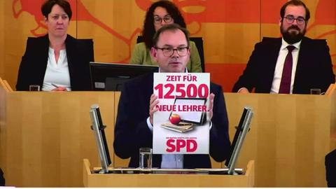 Der Grüne Fraktionsvorsitzende Mathias Wagner hält im Plenarsaal in SPD-Wahlplakat mit der Aufschrift "Zeit für 12.500 neue Lehrer" hoch