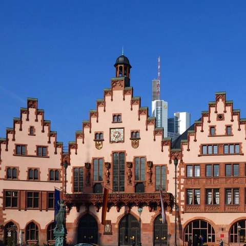 Rathaus Römer in Frankfurt, ein Haus mit drei Gebäudeteilen mit Zinnen, im Vordergrund ein Brunnen im Schatten