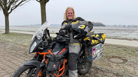 Tristan Duchscherer aus Karben mit seiner KTM - ein junger Mann mit halblangen blonden, leicht gelockten Haaren sitzt auf seinem Motorrad. Er lächelt und trägt Motorrad-Schutzkleidung, den Helm unter dem linken Arm. 