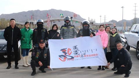 Tristan Duchscherer zu Besuch beim Motorrad-Club in Wuhan. Gruppenfoto - Tristan Duchscherer in Motorradausrüstung mit Helm steht mittig - um ihn herum zehn Menschen, zwei von ihnen kniend. Sie halten ein etwa 1 x 1,5 Meter großes Plakat mit chinesischen Schriftzeichen 