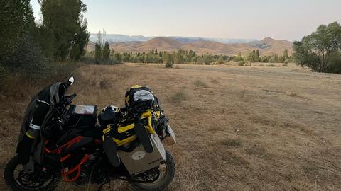 Halt in Bayburt in der Türkei. Das bepackte Motorrad steht auf einer trockenen Steppenfläche, die links und rechts von Bäumen begrenzt wird. Im Hintergrund erhebt sich eine Hügellandschaft.  