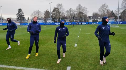 Mehrere Darmstadt-Spieler laufen sich warm. Wegen der kalten Temperaturen tragen sie langärmlige dunkelblaue Trainingsanzüge, Handschuhe, Schals und Mützen. 