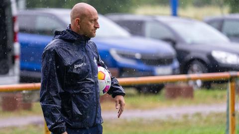 Trainer Torsten Lieberknecht steht im Regen auf einem Trainingsplatz. Er hält einen Fußball in den Händen.