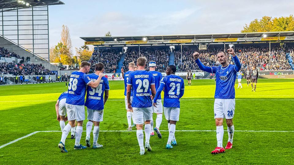 Eine Grupppe von Lilien-Spielern in weiß-blauen Trikots stehen auf einem Fußballfeld und jubeln.