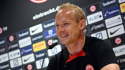 Sebastian Rode sitzt bei einer PK im Trainingslager vor einem Mikrofon und lächelt.