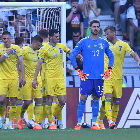 Kevin Trapp mit versteinertem Blick. Im Hintergrund bejubeln die Ukrainer den Treffer.