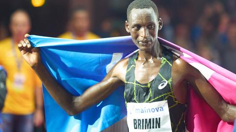 Marathonläufer Brimin Misoi Kipkorir in Trikot mit der Aufschrift "Mainova Brimin 9" hält eine rosa-hellblaue Fahne hoch