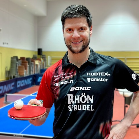 Tischtennisspieler Dimitrij Ovtcharov steht in einer Sporthalle in Fulda und lächelt in die Kamera.