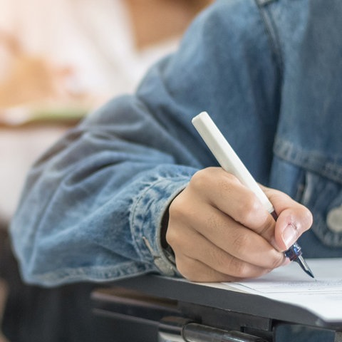 Kind mit weißem Füller in der Hand schreibt in der Schule