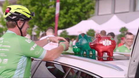 Mann mit Fahrradhelm stellt Glücksschweine auf ein Autodach
