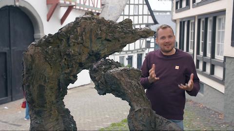 Mann gestikuliert hinter einer Statue