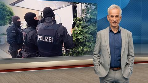 hessenschau-Moderator Andreas Rieke im Studio. Im Hintergrund ein Bild von vermummten Polizisten