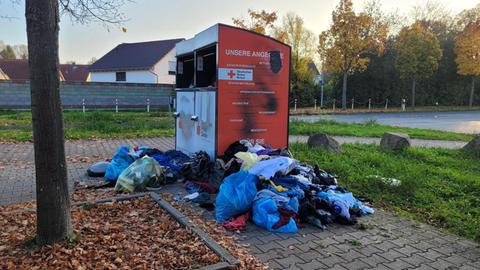 Zwei überquellende Altkleidercontainer vom Deutschen Roten Kreuz stehen auf einem gepflasterten Weg - davor liegen viele Beutel mit Kleidern und Unrat. 