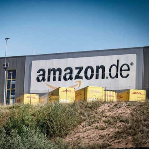 Lagerhalle mit Amazon-Schriftzug, davor gelbe Transport-Lastwagen