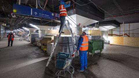 Zwei Männer in Bauarbeiterkleidung stehen vor einer Baustelle.