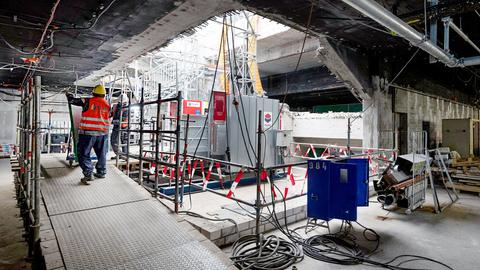 Zwei Männer in bauarbeiter-Kleidung stehen vor einer Baustelle.