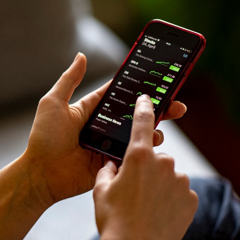 Eine Frau hält ein Smartphone in der Hand, auf dem Börsenkurse angezeigt werden.