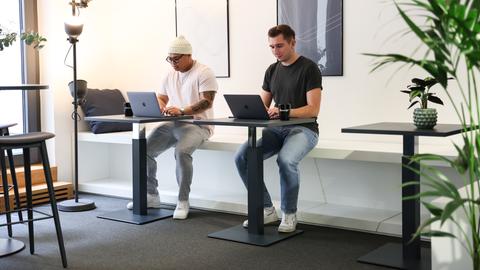Zwei Männer sitzen mit vor ihren Laptops an Tischen.