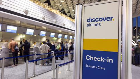 Reisende stehen an einem Check-in-Schalter von Discover Airlines am Rhein-Main-Flughafen