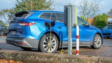 Ein Elektroauto steht auf einem Parkplatz und ist an eine E-Ladesäule zum Aufladen der Batterie angeschlossen