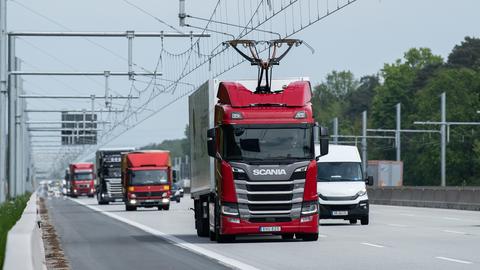 Viele Lkws hintereinander auf einer Autobahn. Oben drüber eine Oberleitung.