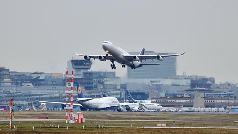 Außenansicht von Gebäuden eine Flughafens und Rollfeld mit einem Flugzeug in der Luft.