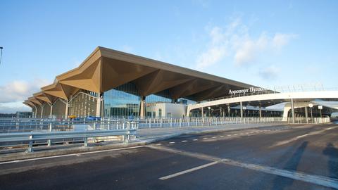 Das Flughafen-Gebäude ist bei Sonnenschein von außen zu sehen, eine große Straße führt dorthin. 