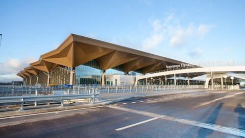 Das Flughafen-Gebäude ist bei Sonnenschein von außen zu sehen, eine große Straße führt dorthin. 