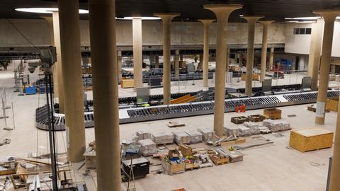 Der Blick in die zukünftige Gepäckhalle zeigt eine sehr hohe Halle mit mehreren Betonsäulen. Rund um die im bau befindlichen Gepäckbänder stapeln sich Werkzeug und Kisten. 