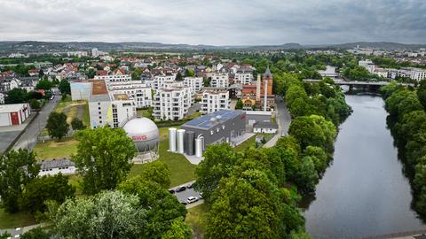 Wir schauen von oben auf die Schlachthofstraße in Gießen. Rechts im Bild verläuft die Lahn. Einige Meter von Fluss entfernt ist ein neues Gebäude zu erkennen. Es ist eine grafische Animation und zeigt die geplante Heizzentrale. Darin werden die neuen Flusswärmepumpen stehen. 