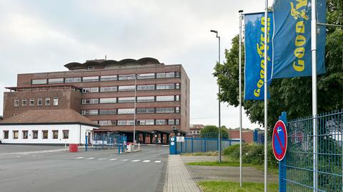 Industriegebäude mit blauen Fahnen davor, auf denen in gelben Lettern "Goodyear" steht.