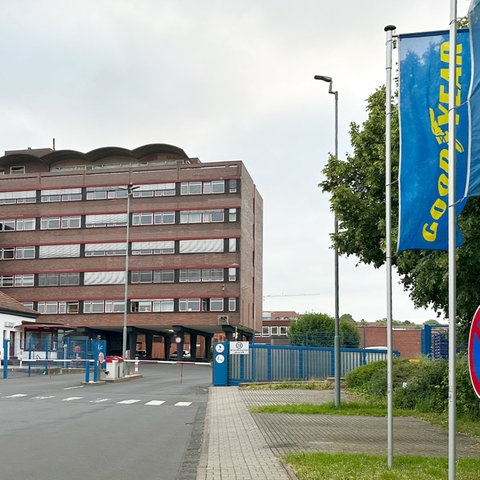 Industriegebäude mit blauen Fahnen davor, auf denen in gelben Lettern "Goodyear" steht.