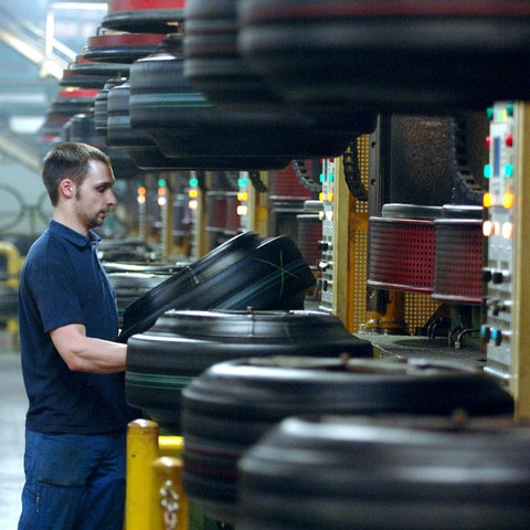 Ein Mann steht in einer Industriehalle an einer Maschine und arbeitet an einem Reifen.