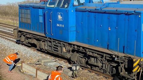 Drei Einsatzkräfte in Warnwesten begutachten eine blaue entgleiste Lok