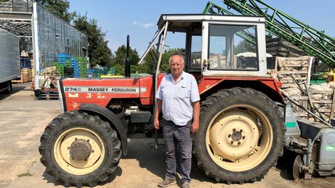 Ein älterer Herr vor seinem Traktor auf einem Bauernhof