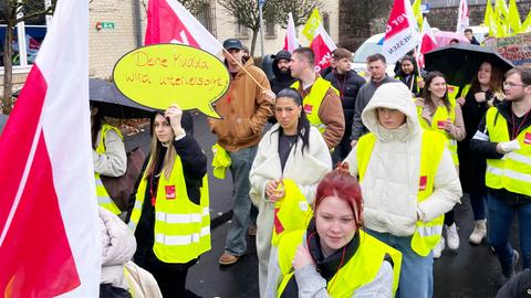 Streikende Azubis mit gelben Warnwesten und roten Trillerpfeifen. Sie tragen Verdi-Fahnen und Plakate mit Aufschriften wie "Deine Mudda wird unterversorgt!".