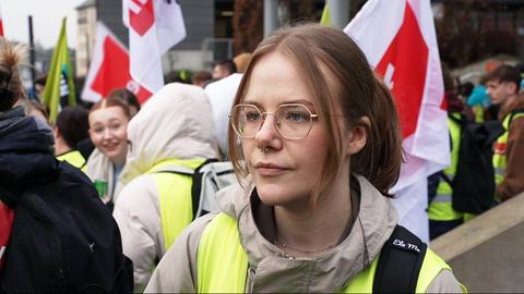 Eine junge Frau mit Warnweste, im Hintergrund weitere Demonstrierende.