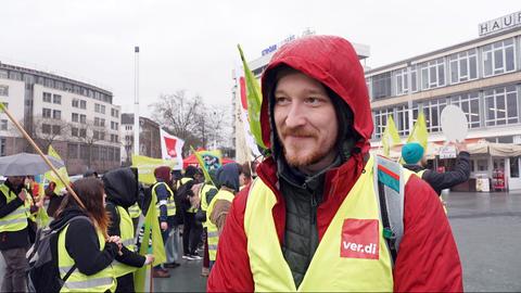 Ein junger Mann mit Warnweste, im Hintergrund weitere Demonstrierende.