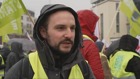 Ein junger Mann mit Warnweste, im Hintergrund weitere Demonstrierende.